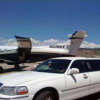 Large white stretch limo parked next to private plane