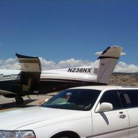 Large stretch white Stagecoach Limo next to private aircraft